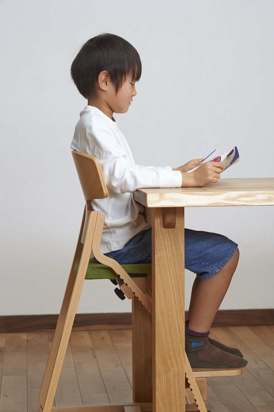 アップライトチェアに座りテーブルで本を読む子どもの横姿